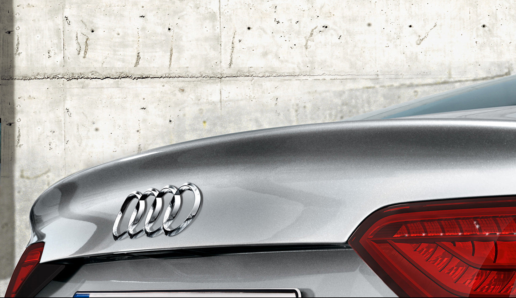 Audi car logo on a car's rear, with a concrete wall background.